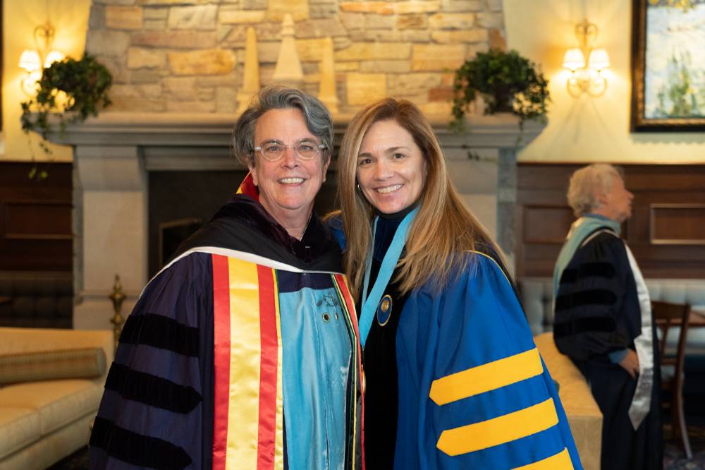 Two faculty members posing for a photo in their academic regalia.